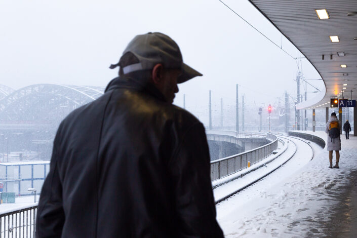 Reisende am Kölner Hauptbahnhof, im Hintergrund die Hohenzollernbrücke bei Schneesturm