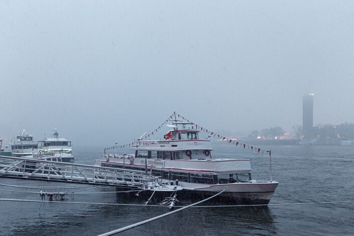 Ein Ausflugsschiff, das an der Rheinuferpromenade angelegt ist; Im Hintergrund das linksrheinische Ufer im Nebel