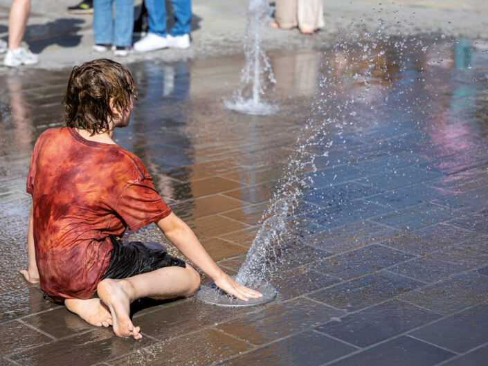 Street-Fotografie: Kind beim Spielen mit einem Wasserbrunnen