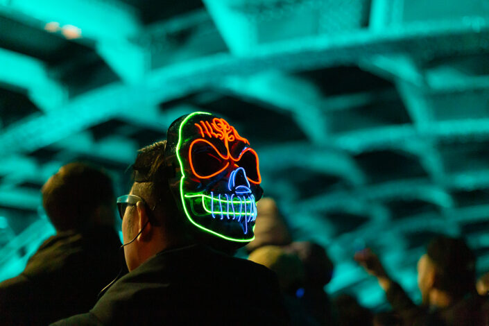 Ein Teilnehmer des Geisterzug 2024, der eine leuchtende Maske in Totenkopfform trägt