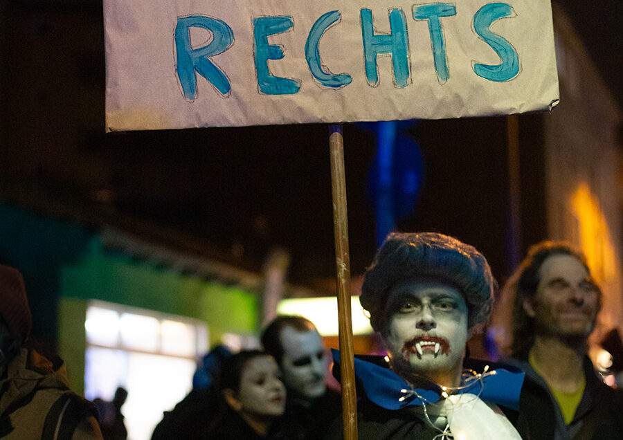 Ein als Vampire verkleideter Teilnehmer, der ein Plakat mit der Aufschrift "Vampire gegen Rechts" hält