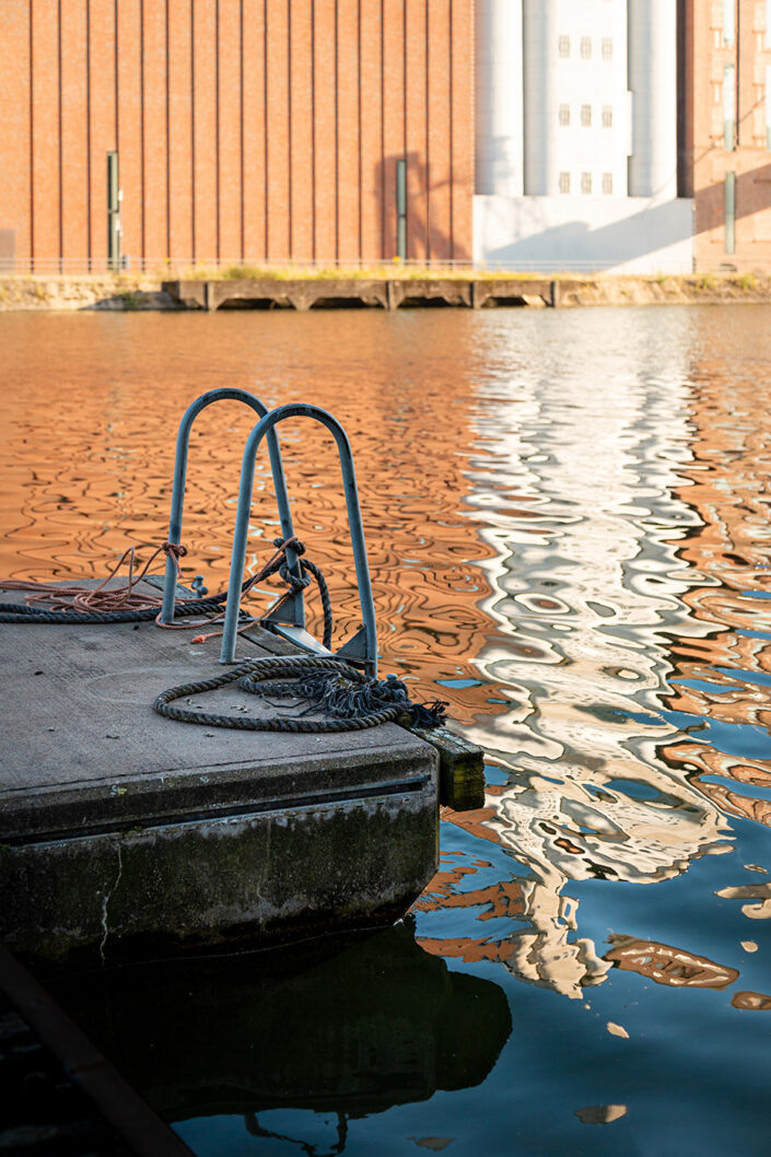 Steg mit Einstiegsleiter im Duisburger Innenhafen, Spiegelungen auf der Wasseroberfläche.